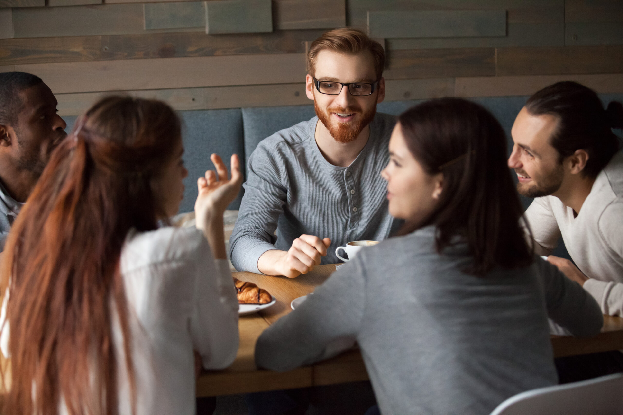 Diverse young people talking and having fun together in cafe, girls chatting sharing coffeehouse table with multiracial friends, multi-ethnic millennials enjoying pleasant discussion in public place